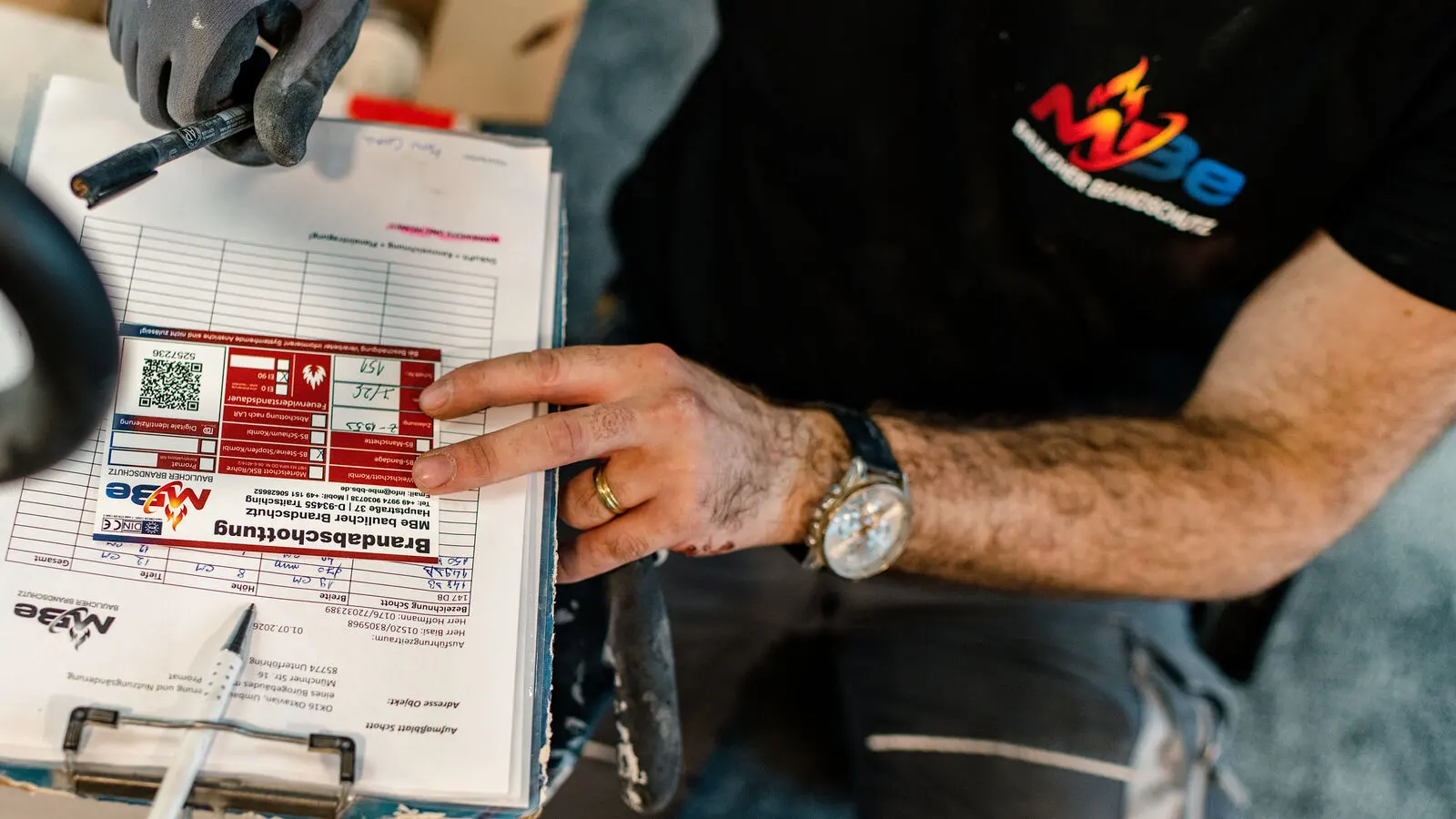 Monteur von MBe Baulicher Brandschutz zeigt auf das Kennzeichnungsschild einer Brandabschottung mit QR-Code.
