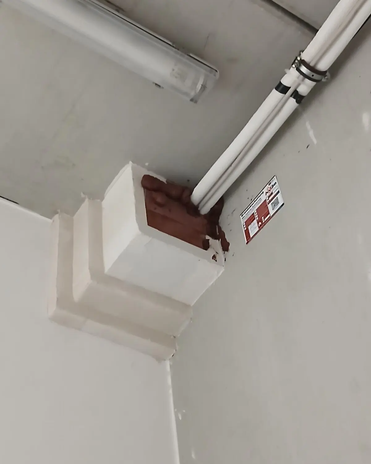 Mit Brandschutzmörtel verschlossene Leitungsdurchführung an einer Kellerdecke, daneben das Kennzeichnungsschild von MBe Baulicher Brandschutz.