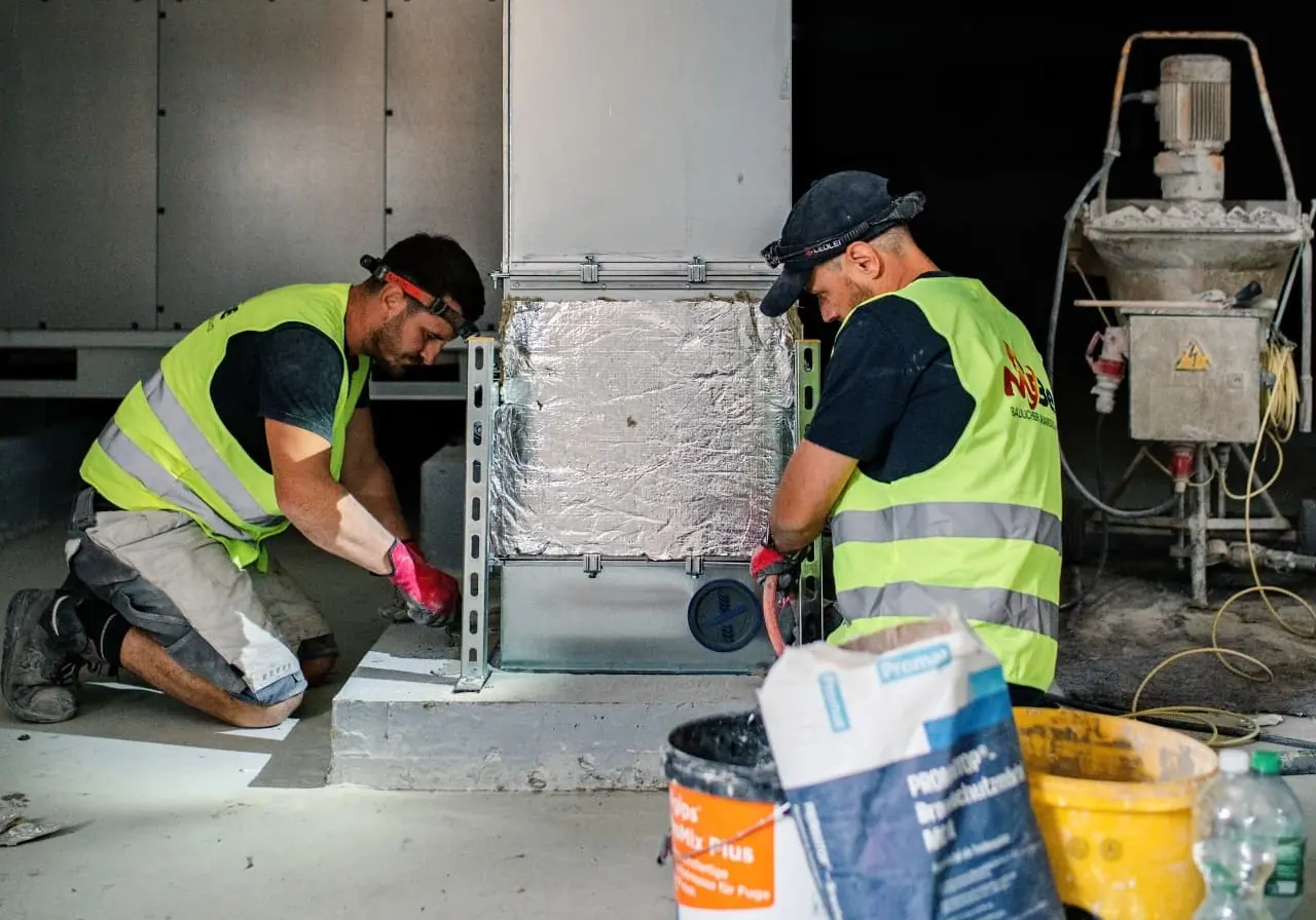MBe-Monteure schotten einen Lüftungskanal in einer Industriehalle ab
