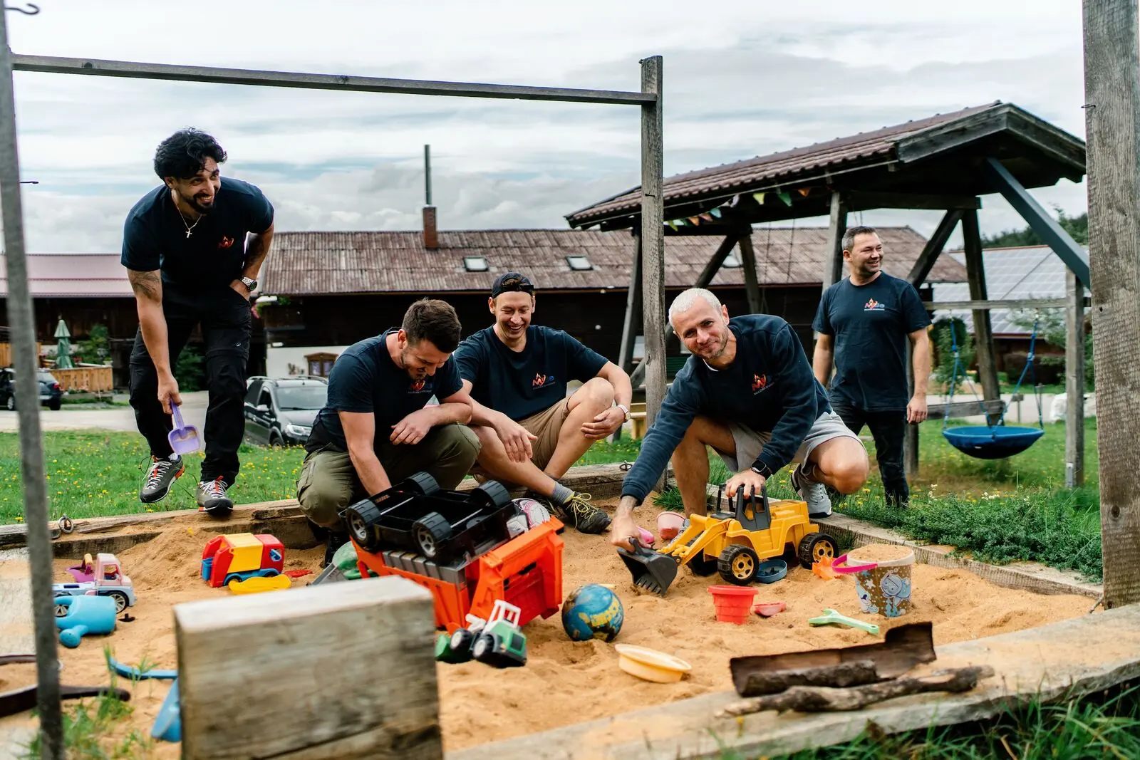 Kollegen spielen beim Teamtag mit Spielzeugbaggern im Sandkasten