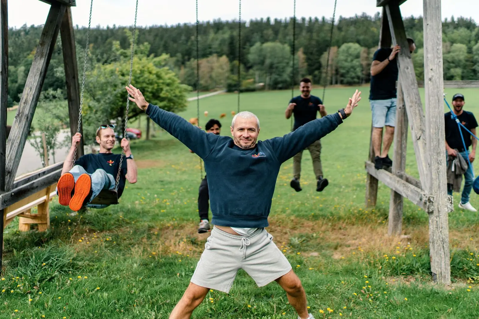 Ein Kollege jubelt beim Teamtag an der Schaukel, im Hintergrund das Team